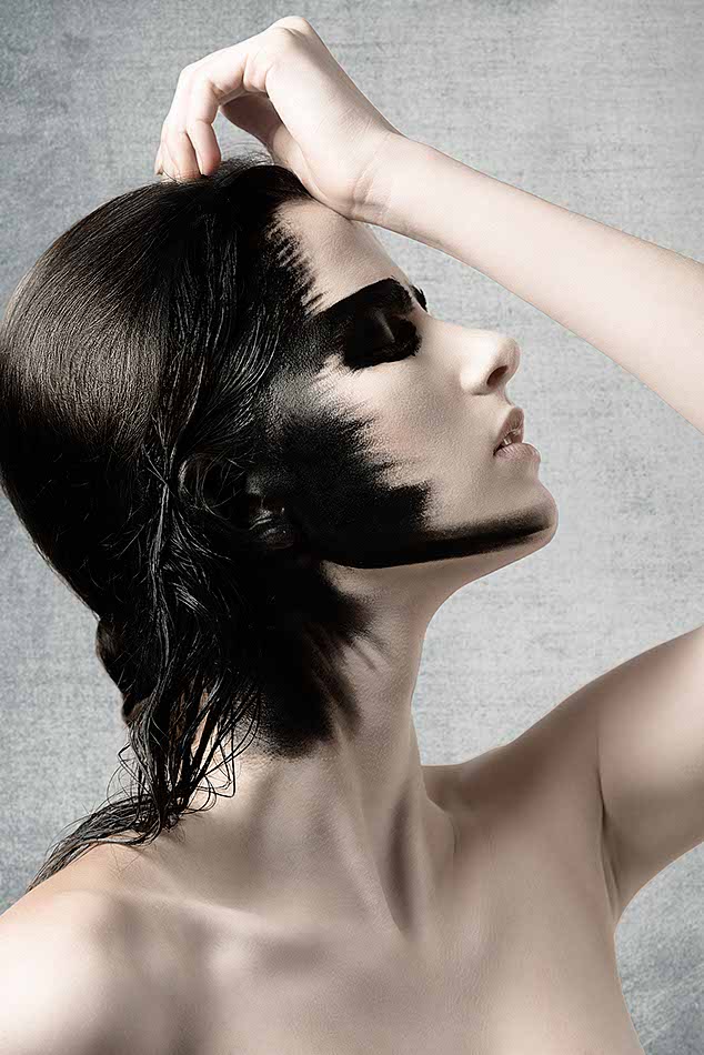 gorgeous woman in theatrical pose in beauty portrait with perfect skin and creative black painted make-up on her visage and on her hair