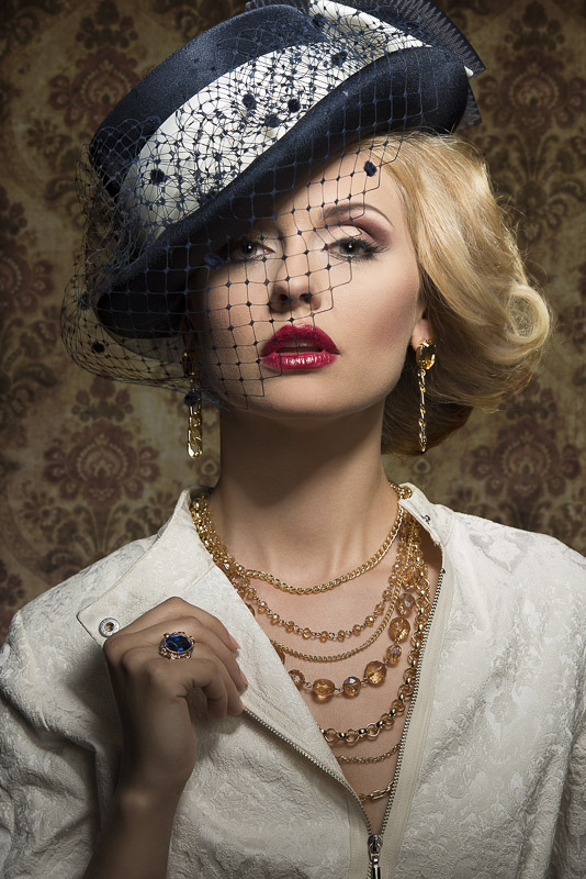 Young,blonde beautiful woman with style in expensive,gold jewelry in smart, blue hat with veil.